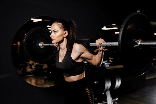 Close-up photo of confident woman doing squats exercises with heavy barbell in the gym