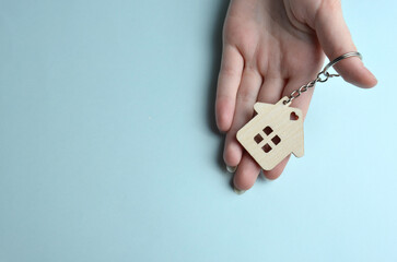 Keychain in the shape of a house on the palm of your hand on a blue background.