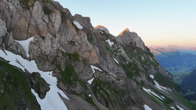 9 juli 2024, Wildhaus, Switzerland. Hovering, Drone flight, during sunrise in Alpstein mountains. Impressive mountains with some snow, amazing purple, red and orange colors during sunrise. Wonderful A
