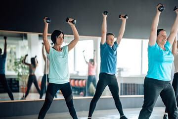 Fitness group exercising with dumbbells indoors. Team motivation and healthy living in an urban gym setting