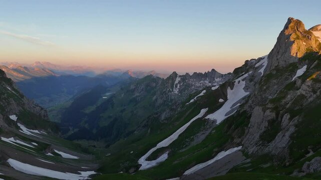 9 juli 2024, Wildhaus, Switzerland. Forward Drone flight, during sunrise in Alpstein mountains. Impressive mountains with some snow, amazing purple, red and orange colors during sunrise. Wonderful Alp