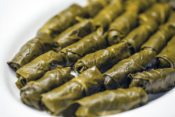 Close-up of tightly rolled, glossy dark green yaprak sarma, a traditional Turkish dish, arranged on a white dish.