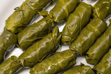 Close-up of tightly rolled, glossy dark green yaprak sarma, a traditional Turkish dish, arranged on a white dish.