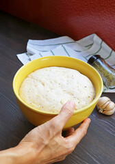 Man's hand placing a mixing bowl of fluffy risen dough on kitchen table