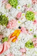 Young woman holding shower gel on background of flowers. Moisturizing shower gel with floral scent.