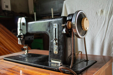 Side view of antique black sewing machine placed on polished wooden table. The design highlights a timeless tool used in traditional tailoring and fabric work.