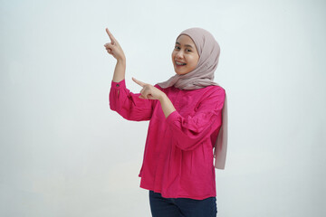 Smiling Young Asian Muslim Woman in Hijab Pointing with Both Hands on isolated background