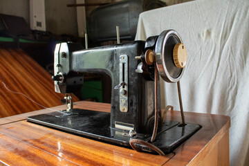 Angled view of vintage black sewing machine on wooden table with white cloth backdrop. Represents heritage, craftsmanship, and home-made garment traditions.