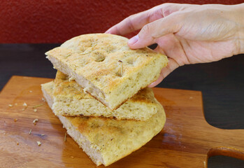 Hand Picking a Slice of Tasty Rosemary Focaccia Bread Piled Up on Wooden Breadboard