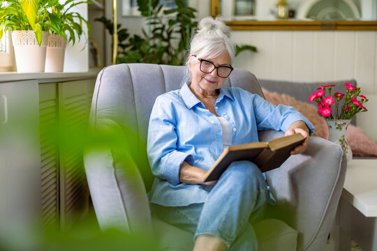 Mature woman reading a book in a comfortable armchair at home
