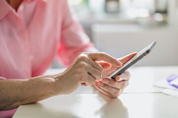 Close-up of an elderly woman's hands using a mobile phone at the kitchen table