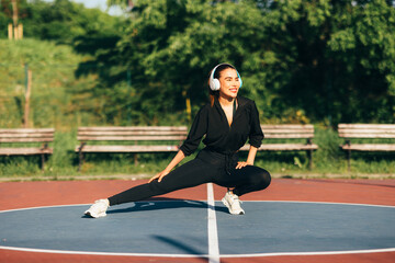 Fit woman doing stretching exercises while listening to music with headphones in an outdoor...