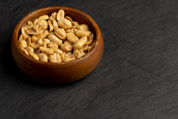 peanuts in a wooden round bowl, crunchy peanuts without shells on a black slate board, closeup