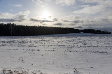an agricultural field under snow in the cold winter in cloudy weather, clouds in the sky, landscape
