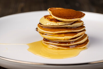 pancakes stacked together on a white bowl, a tower of small milk pancakes on a ceramic bowl with bee honey, closeup