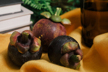 Lush still life set up with three purple Mangosteen, a stack of books, green vines, vibrant yellow...