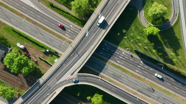 Top-down drone rotating view of multilane road and curved overpass intersecting railway tracks in green urban environment