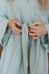 A woman dressed in a light blue robe is carefully tying a belt around her waist, showcasing the beauty of her attire