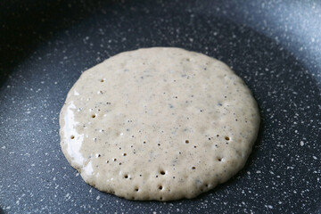 A healthy whole wheat flour with ground black sesame seeds pancake being fried in pan
