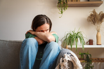 Sad woman sitting in fetal position while feeling emotionally overwhelmed at home