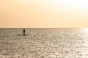 Fototapeta premium Person paddleboarding alone in calm sea at sunset. Summer postcard. Vacation. Loneliness. Rest.