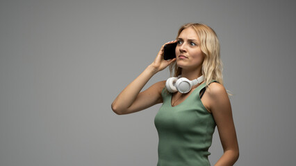 Confused young woman talking on smartphone with headphones around her neck