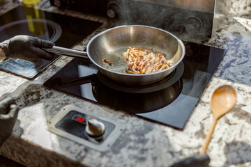 A chef cooks bacon in a stainless steel pan on a sleek countertop stove, showcasing culinary skills.