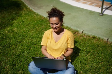 Smiling Woman Using Laptop Outdoors in a Green Park Setting