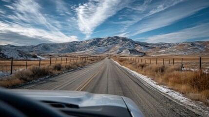 Looking out the car window reveals a breathtaking view of a winding road surrounded by mountains and rolling hills under a vibrant blue sky. This peaceful moment captures nature's beauty