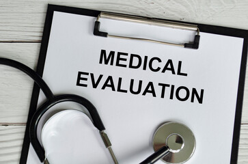 Top view of Medical Evaluation Text on white paper clipboard with stethoscope on wooden table...