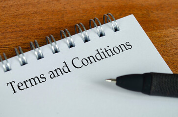 Obraz premium Terms and Conditions text on white notepad with wooden table background. Terms and Conditions and business concept.