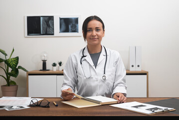 In her office, a smiling female doctor addresses the camera, greeting patients warmly during an online appointment