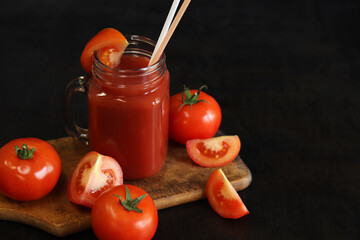 Tomato juice on a dark background. Vegetable diet drink. Fresh tomato juice in a glass with a handle. Ripe red tomatoes and juice made from them. Glass with juice and a straw, tomatoes. Healthy drink