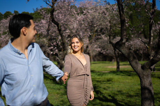 Happy latin couple holding hands and walking in blossoming park - Powered by Adobe