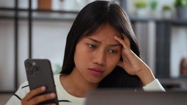 Young asian woman sitting at home looking confused and concerned while reading smartphone screen, concept of unexpected news, online problem, or misunderstanding