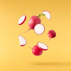 Fresh raw Red Radish with green leaves falling in the air isolated on yellow backgriund. Food...