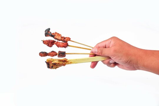 a hand hodling four type of satay skewers (Sate Tusuk) including tuna, pork, chicken, and lilit made with Balinese style traditional street food