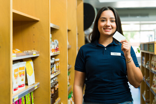 Happy supermarket employee showing blank card in grocery store