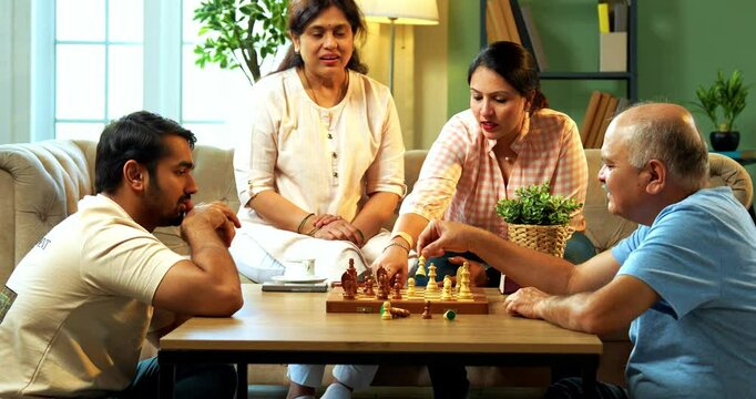 Playing chess at home on sofa, Indian family of four including senior parents and young adult son and daughter enjoy quality time in modern cozy living room, bonding over intelligent board game fun