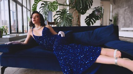 sexy woman fashion model posing in blue long dress evening gown white gloves old style. Glamour Retro lady beauty girl girl lies on stylish sofa. Wavy black hair holiday concept themed party new year