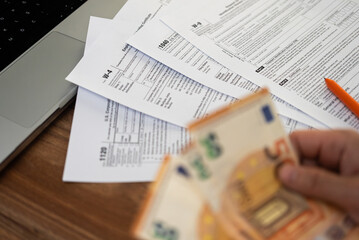 Obraz premium Accountant hand holds euro banknotes preparing financial information for filling various tax forms in compliance with law at workplace with laptop in company office