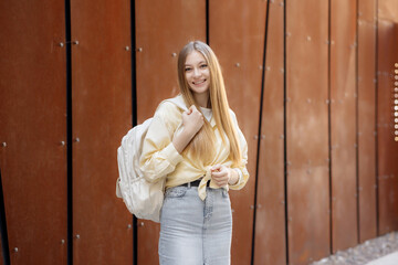 Fototapeta premium Young woman with long hair and backpack smiles in front of modern urban architecture during daytime