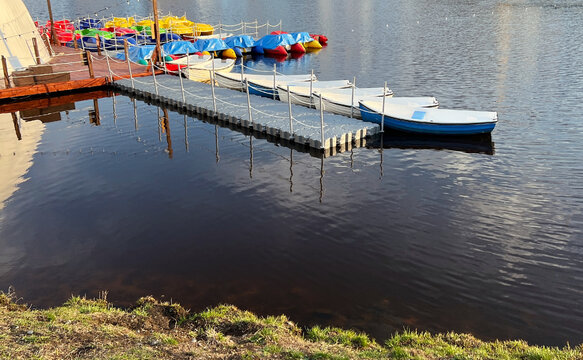 Brightly colored paddle boats are arranged neatly at floating dock next to a calm lake on a clear day