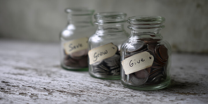 Three glass jars filled with coins, labeled "Save," "Grow," and "Give," sit on a rustic wooden surface, representing financial planning, savings, investment, and charity