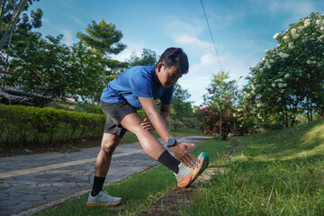 Asian man stretching his legs before a morning run in a city park, preparing for exercise with an...
