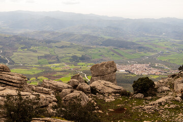 Scenic rocky landscape view from El Torcal de Antequera, Spain. Limestone rock formations rise above green valleys and distant mountains under a partly cloudy sky in Antequera, Spain.