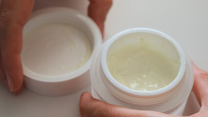 Two hands reveal a jar of creamy skincare product, showcasing a smooth texture for hydration....