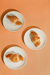 Flat lay of coffee cup and fresh croissants on orange  background with shadow. Creative layout and concept of healthy food and french breakfast. Top view. 