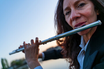 close up of a middle aged female face playing a transverse flute at sunset on a small pier