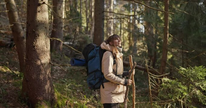 Girl in hiking clothes with big backpack walking in forest and enjoying views during her journey in wild forest. Rest in the Sunny Forest during the hike